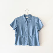 Light Indigo Blue button-up petite t-shirt with collar, visible waistline like a subtle peplum, darts for fitting and covered buttons.