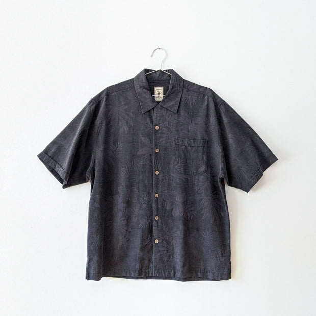 Charcoal grey button-up tropical print silk t-shirt with brown wooden buttons, one chest pocket and collar. 