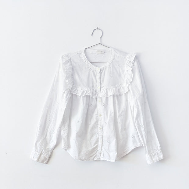 White eyelet button-up blouse, cotton, Victorian style, crew neck, long sleeve with a square ruffle above the chest and below the neckline.