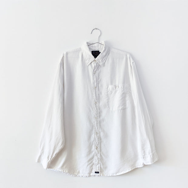 White linen button-down long sleeved collared shirt with two chest pockets that button.