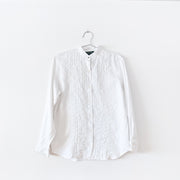 White linen long sleeve button-up shirt with mandarin collar and brass button. There is vertical pleating and white ladder lace at the center front. Secondhand Lauren Ralph Lauren, from Fold and Fray.