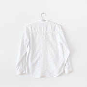 The back of a White linen long sleeve button-up shirt with mandarin collar. It has white ladder lace trim and vertical pleating down the center back. Secondhand Lauren Ralph Lauren, from Fold and Fray.