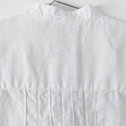 Close-up on the back of white linen long sleeve button-up shirt. The mandarin collar has a button hole. Under the back yoke there is white ladder lace trim and vertical pleating down the center back. Secondhand Lauren Ralph Lauren, from Fold and Fray.