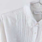 Close-up on a white linen long sleeve button-up shirt. Shows white lace ladder trim and pleating on the front.  Liz Claiborne Lizsport. Secondhand from Fold and Fray.