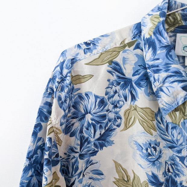 Vintage Jessie Blue Floral Button-up Long Sleeve Shirt. Shoulder Close-up: Blue Flowers, Green Leaves, Off-White Background.