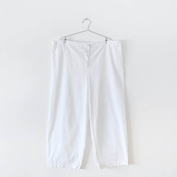 White cotton pyjama pants with straight leg and drawstring and elastic waist, with the waist fully extended to show full width. Secondhand gender and size inclusive clothing from Fold and Fray.