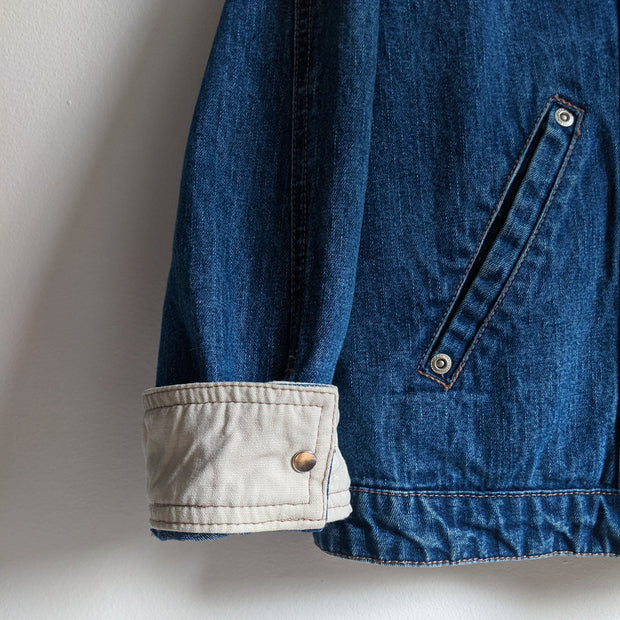 Cotton button-up denim jacket in Indigo Blue with collar, close up of beige lined cuff with snap closure.