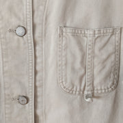 Close-up detail of small breast patch pocket on cotton, field-style, barn jacket, chore coat in Sand Beige (like a greige, tan). Show the metal buttons that say "Eddie Bauer." Eddie Bauer Women's. Secondhand, from Fold and Fray.