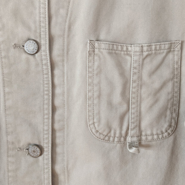 Close-up detail of small breast patch pocket on cotton, field-style, barn jacket, chore coat in Sand Beige (like a greige, tan). Show the metal buttons that say "Eddie Bauer." Eddie Bauer Women's. Secondhand, from Fold and Fray.