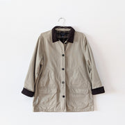 Cotton canvas field-style barn jacket, chore coat in Sand Beige (like a greige tan). It has dark brown buttons and dark brown corduroy lined collar and cuffs. The inside of the jacket's torso is lined with green plaid flannel. This jacket has four exterior pockets: two lower patch pockets with flaps and two upper angled welt pockets. Land's End. Secondhand from Fold and Fray.