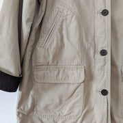 Close up of cuff, pockets and buttons on cotton canvas field-style barn jacket, chore coat in Sand Beige (like a greige tan). It has dark brown buttons and dark brown corduroy lined cuff. This jacket has four exterior pockets: two lower patch pockets with flaps and two upper angled welt pockets. Land's End. Secondhand from Fold and Fray.