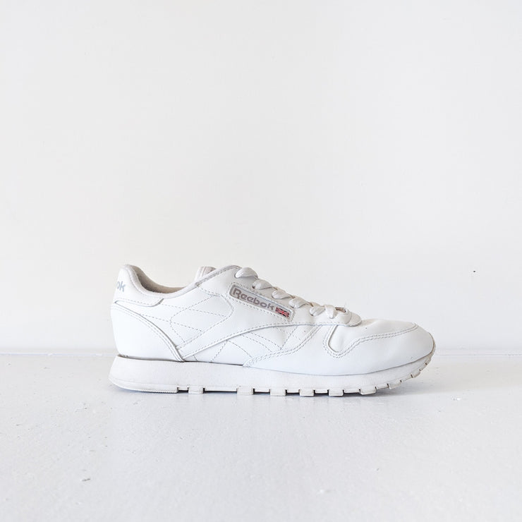 Side view of one White leather Reebok classic lace-up sneaker with white sole.