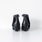 Back heels of Black leather heeled ankle booties with almond toe. The top of the boot is shown roll down down over western-style fringe on the outer side of the boot. Sam Edelman Black Louie Boot 8M. Secondhand from Fold and Fray.