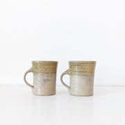 Two Tan/Brown Speckled Ceramic Mugs, Rough Texture. Top Third has Darker Yellow Glaze. Shape Opens Wider at Mouth.