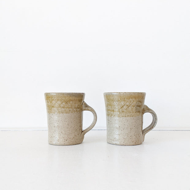 Two Tan/Brown Speckled Ceramic Mugs, Rough Texture. Top Third has Darker Yellow Glaze. Shape Opens Wider at Mouth.